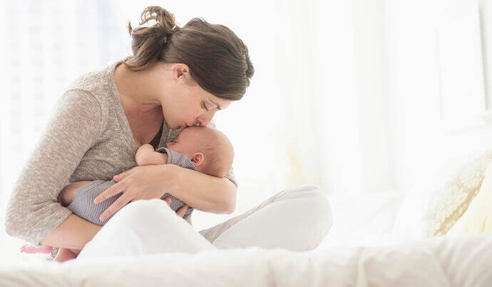 woman holding baby and kissing its forehead