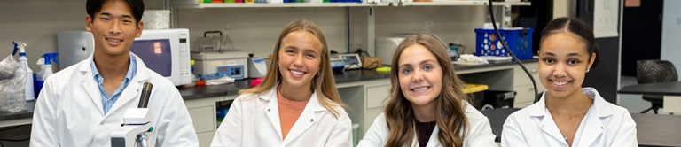 Four high schoolers smiling in lab coats.
